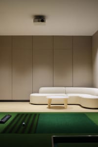 A modern interior living room with a white sectional couch, a round wooden table, and a projector hanging from the ceiling.
