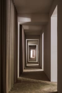 A minimalist corridor with neutral-toned walls and curtains, featuring repetitive architectural elements.