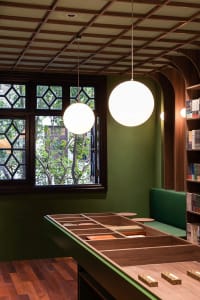A modern cafe space with wooden shelves, green walls, and spherical hanging lights.
