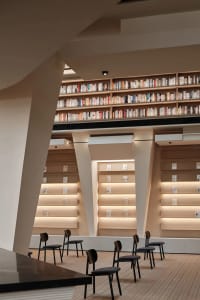 A minimalist library with wooden shelves filled with books and illuminated by soft lighting.