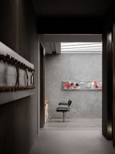 A minimalist barber shop interior featuring a concrete wall with a black and red graffiti piece above a black barber chair.