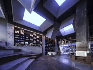 A minimalist library interior with modern concrete architecture, featuring skylights and bookshelves.