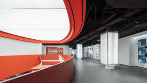 Modern office lounge area with red walls, concrete flooring, and curved architectural elements.