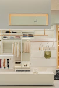 A clothing retail store with neutral-toned decor, featuring shelves and hanging garments.