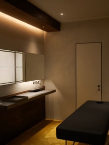 Modern minimalist medical office room with concrete floor, wooden walls, and a black leather patient bed