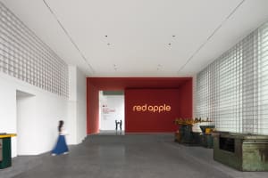 A modern industrial-style office space featuring concrete walls and floors, with a red accent wall and large windows.