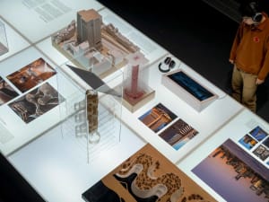 A display of architectural models and photographs in a museum or exhibition setting.