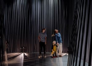 Three people standing in front of a modern art installation featuring a curtain of metal rods