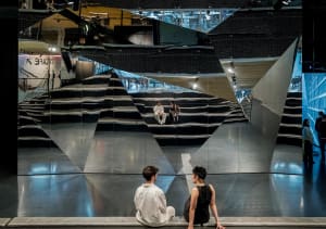 Two people sitting in a modern performance space with reflective mirrors.