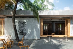 Modern minimalist restaurant exterior with concrete walls and open seating area under palm trees.