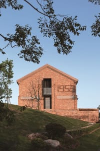 A minimalist building with brick exterior on a grassy hillside.