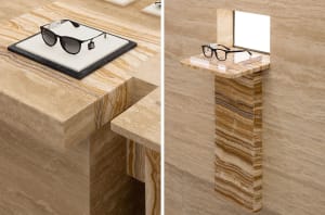 A stylish retail display featuring black sunglasses and a clear spectacle frame placed on a marble surface and pedestal.