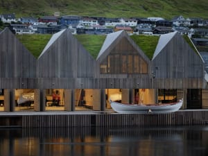 Modern wooden architectural structure with green roofs and boats docked in the water.