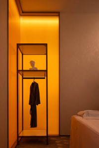 Clothing studio with an open metal cabinet featuring a robe hanging inside and a bust statue on the top shelf.