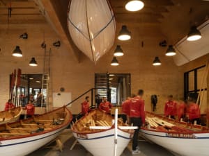 People working in a modern boating center with boats, oars, and wooden structures.