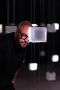 Person leaning on a modern glass box installation in a dark space.
