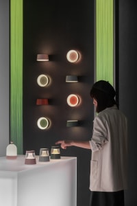 A woman selecting different colored lighting fixtures on a display table in a dark room with green vertical accents.