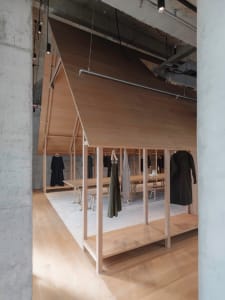 Minimalist clothing store with wood walls and floors, featuring clothing racks.