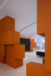 A modern office space featuring orange cube structures, white walls, and a concrete floor.