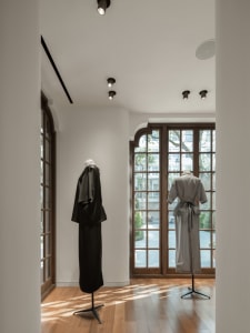 A modern retail space featuring clothing on mannequins in a store with large windows, wooden flooring, and minimalist decor.