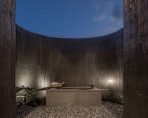A minimalist bathroom with concrete walls, a stone floor, and a simple vanity and sink.