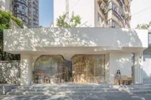 Modern retail storefront with white concrete exterior and glass windows, surrounded by greenery.