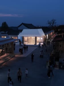 A modern cultural center with a glass facade and open interior space illuminated by warm lighting.