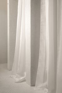 A minimalist public bathroom with white tiles and white fabric dividers.