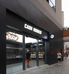 A modern retail storefront with black glass walls and a neon sign displaying 'Cash Hooked'.