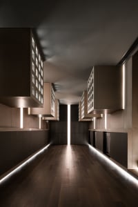 A minimalist corridor featuring wooden panels, metal accents, and illuminated lighting.