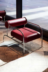 A modern red leather accent chair with a metal frame, placed in front of a large window.