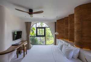 A minimalist bedroom featuring a white bed with a wicker headboard and wooden desk area.
