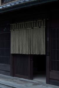 A traditional Japanese storefront with a rope curtain hanging from above.