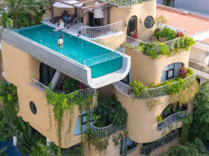 Scenic view of a modern residential building exterior with a large infinity pool on the roof, surrounded by greenery and arch
