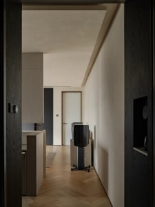 A modern residential interior featuring herringbone wood flooring, minimalist furniture, and a sleek, contemporary kitchen de