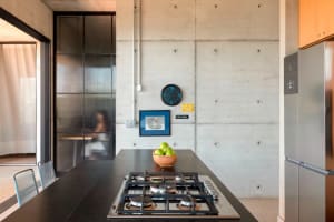 A modern, industrial kitchen with concrete walls, a black countertop, a stainless steel stove, and a bowl of green apples.