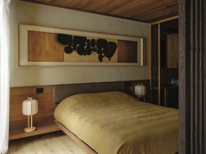 A modern bedroom with wooden elements and a minimalist aesthetic features a large bed with a soft, textured quilt, two lanter