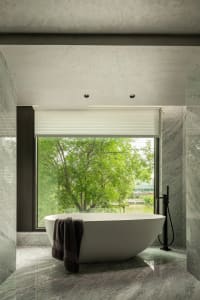 A modern bathroom features a freestanding tub surrounded by marble walls and floors, with a window overlooking lush greenery 