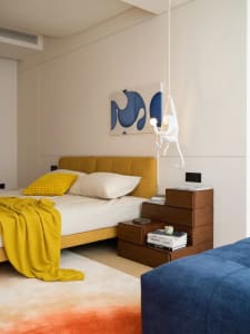 Modern minimalist bedroom featuring a yellow upholstered bed, wooden nightstands, and a creative hanging monkey light fixture