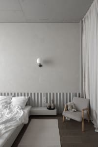 Minimalist bedroom with concrete and wood materials, featuring white bedding and a floating nightstand.