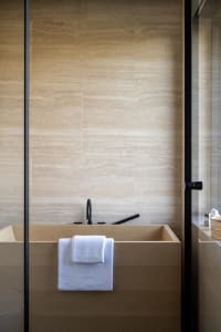 Modern minimalist bathroom with a wooden soaking tub, white towels, and a tiled wall