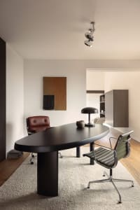 A modern office setting with a black wooden desk, leather chair, and rug, featuring brick walls and a ceiling light.