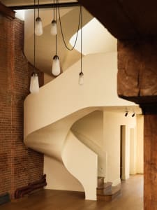 A spiral staircase with white plaster walls and wooden railings and steps