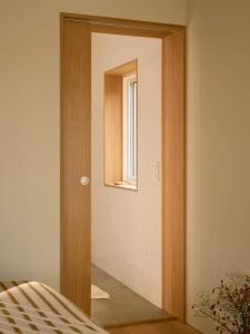 Modern minimalist bathroom with white walls, a wood door, and a small window.