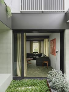 A modern living room with concrete walls and floor, featuring a large sofa, green carpet, and a green plant.