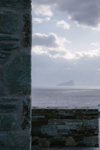 A view of the ocean from a stone structure, with clouds in the sky and an island in the distance.