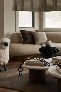 Comfortable beige sofa with dark brown textured cushions and a plush white sheep figurine in a cozy living room setting.