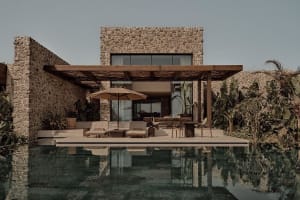 Modern residential exterior featuring stone walls, concrete patio, and a tranquil poolside area.