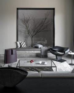 A modern interior design featuring a concrete bench with glass inserts, a black leather armchair, and a glass table.