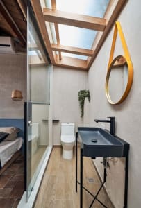 A modern bathroom with concrete walls, a glass shower enclosure, and a black sink with a yellow mirror.